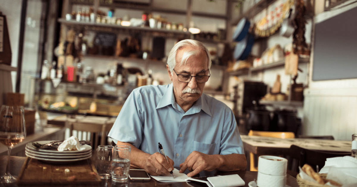 Senior man reviewing financial documents in a cafe, considering an unsecured line of credit for business needs.