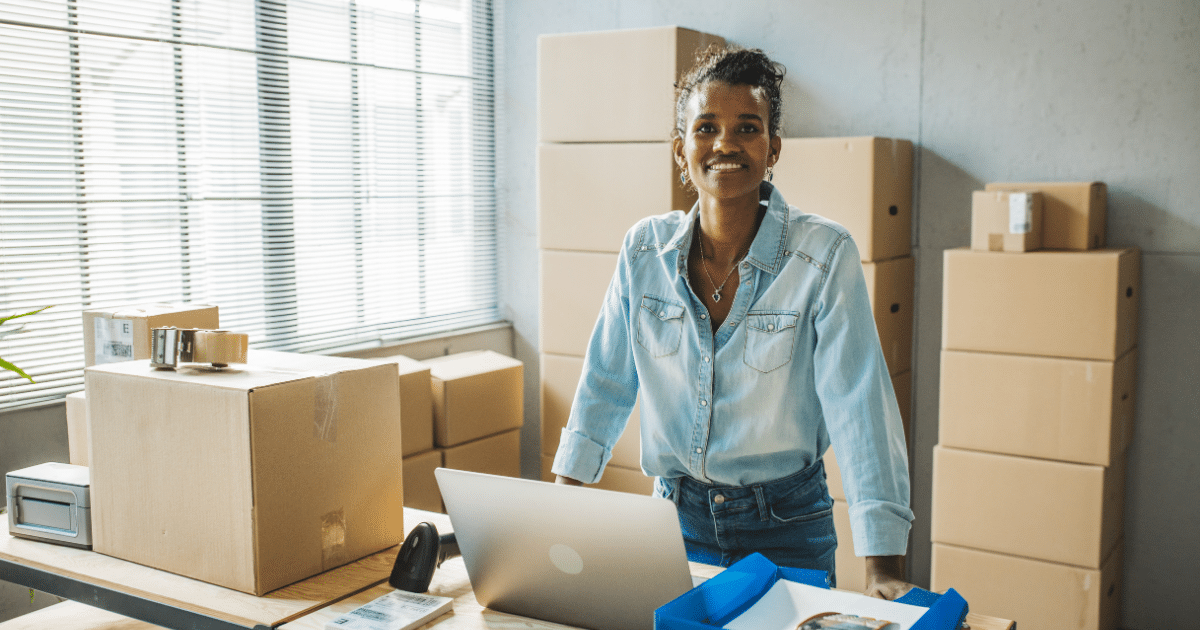 Smiling woman in a workspace with boxes and a laptop, representing optimized medical accounts receivable solutions.