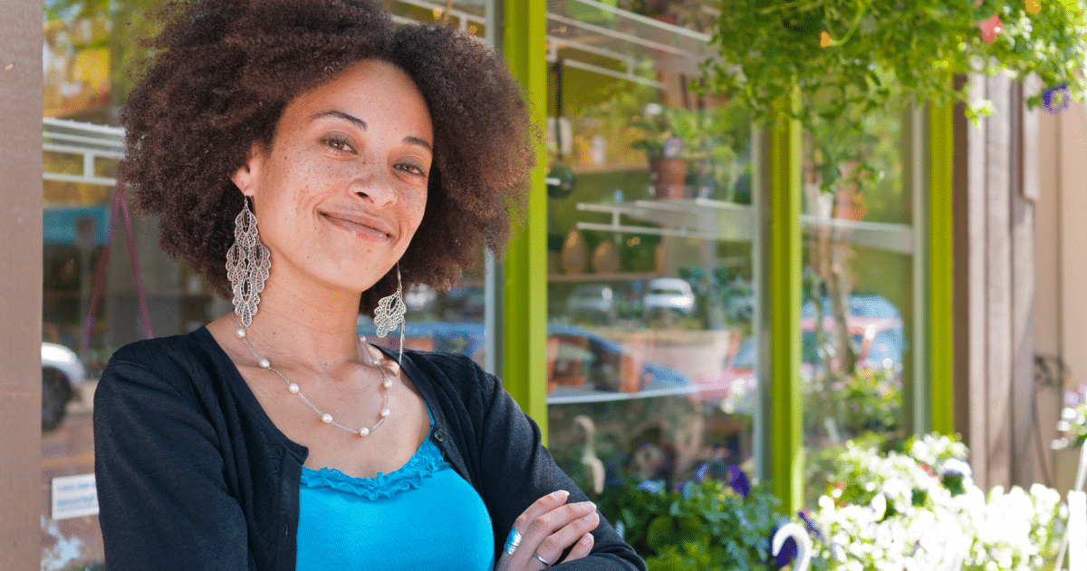 Smiling businesswoman in front of a shop, representing smart financing and networking for business growth.