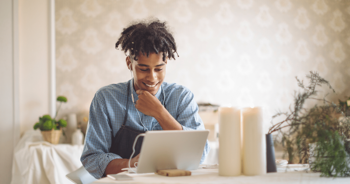 Smiling man using a laptop at a table with candles, representing efficiency in trucking and logistics tools.