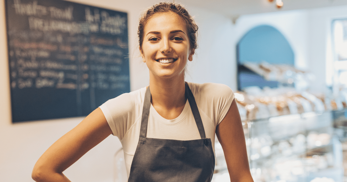 Smiling business owner in an apron, representing small business growth and loan potential in a cafe setting.
