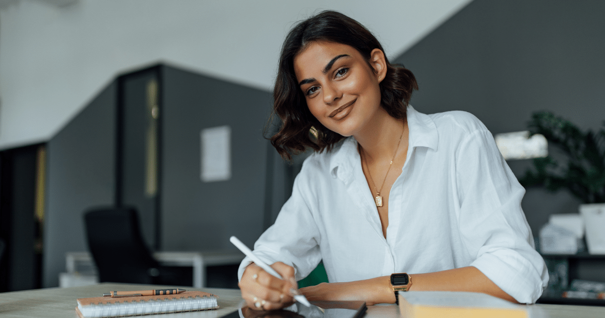 Young entrepreneur smiling while writing notes in a modern office, embodying business success and creativity.