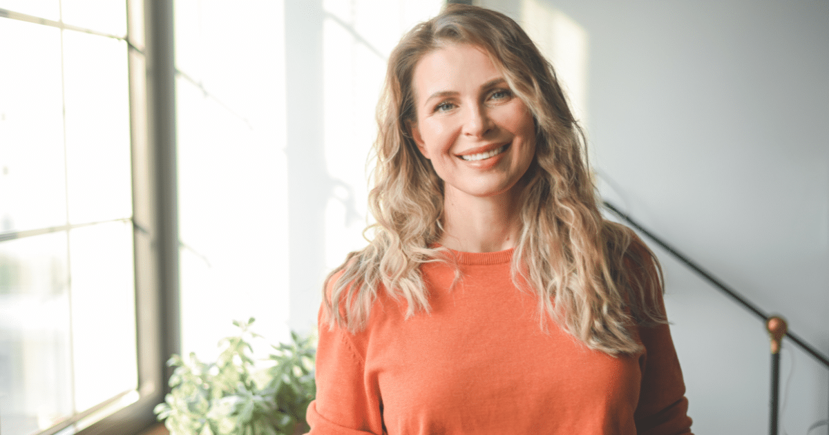 Smiling woman in an orange sweater, representing entrepreneurship in small business niches like translation and green construction.