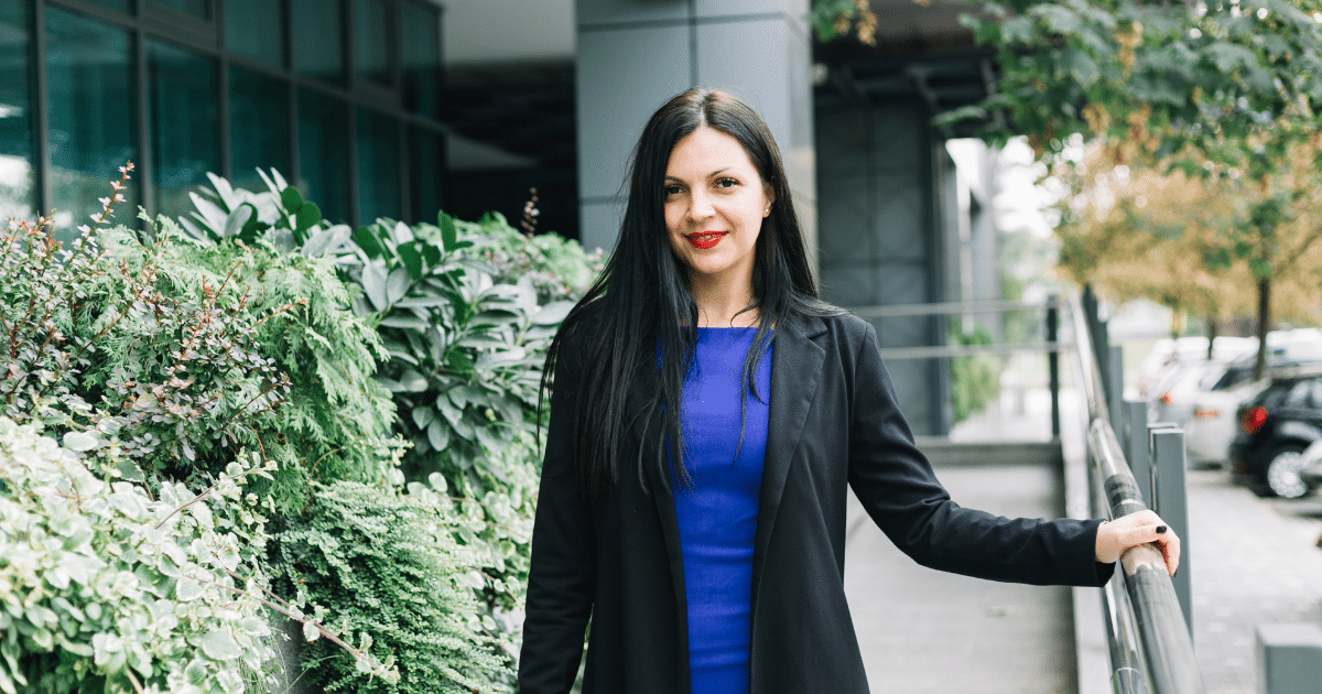 Business professional in a blue dress and black blazer standing outdoors, promoting customer retention strategies for growth.