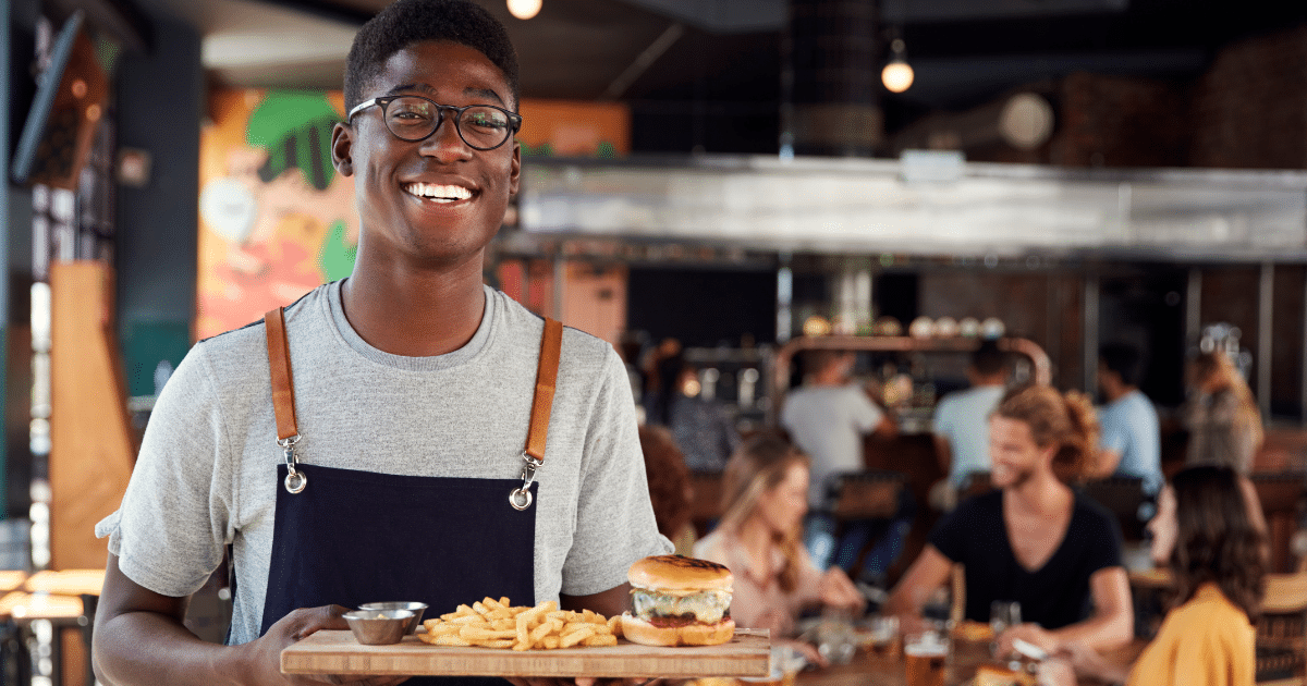 Smiling restaurant server holding a burger and fries, showcasing restaurant dining experience and financing opportunities.